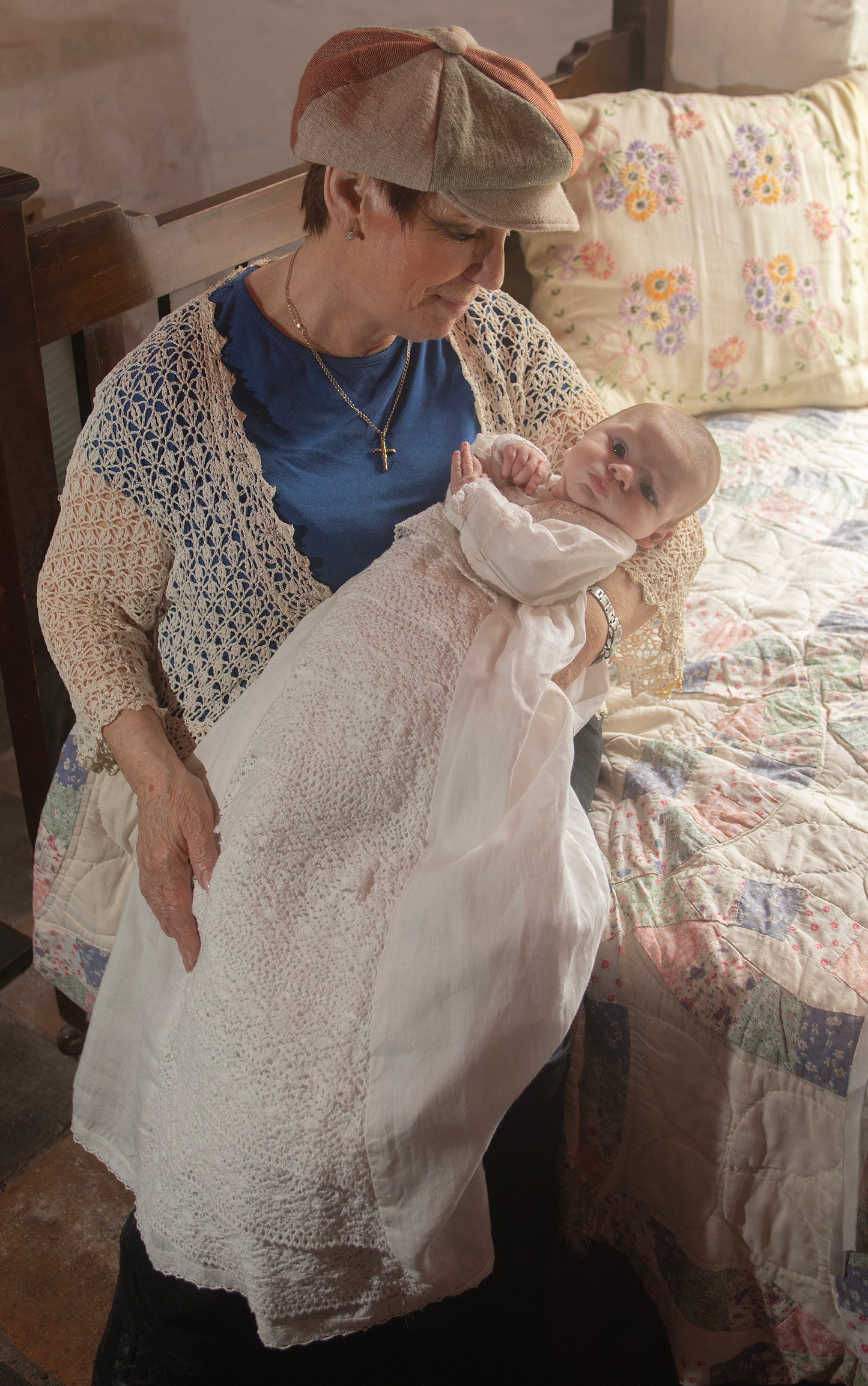 Woman holding a baby in Aoibhe CHristening Gown in a bedroom setting.