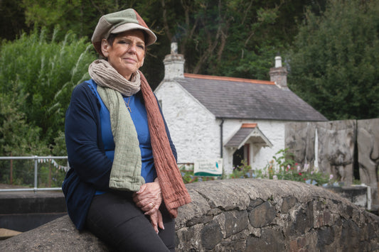 Woman sitting on a stone wall with a house and garden in the background