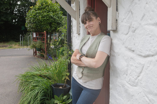 Woman leaning against a white cottage wall with plants around
